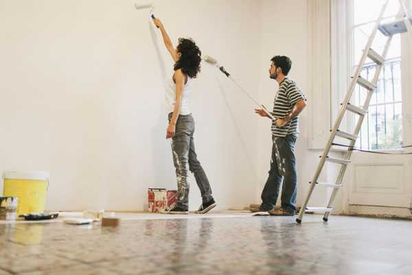 Male and female paining a wall white with the use of rollers