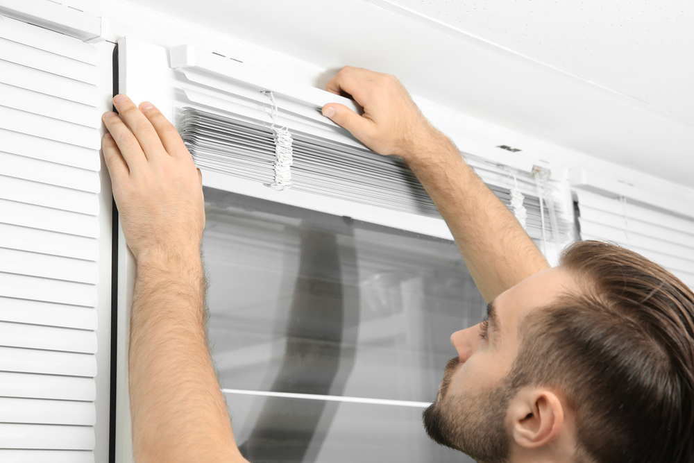 Male installing small set of white blinds on a white window frame