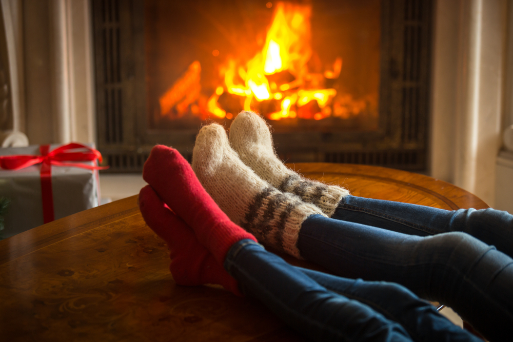 2 pairs of feet in woolly socks resting on a coffee table in front of a fire