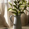 a plant in a white vase next to a book